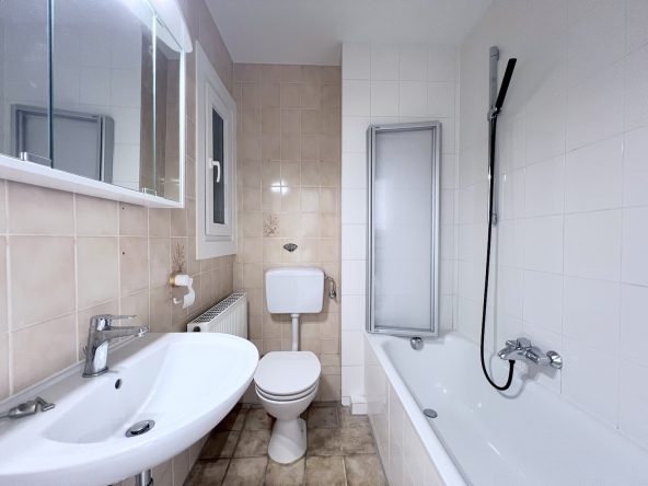 Badezimmer mit Wanne, Wc, Waschbecken und Spiegelschrank, hell gefliest